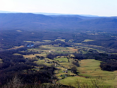 [The valley has a lot of open green-grass land with some sections of trees. There are a number of homes scattered across the grassy areas. In the distance is the tree-covered mountain.]